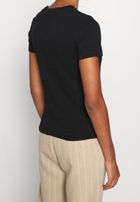 Svart t-shirt med korta ärmar och rund halsringning. Bakdelen har en liten sömdetalj. Matchas med beige randiga vida byxor.