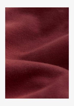 Țesătură burgundy cu o textură netedă, având un model fin de tricot. Materialul pare ușor șifonat, evidențiind pliul său moale.