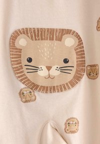 Vaalean beige-kangas, jossa on suuri leijonan kasvomalli, jossa on teksturoitu harja ja pienempiä leijonamalleja ruskean sävyissä.