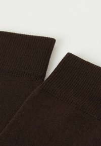 Brązowe skarpety dzianinowe z prążkowanymi mankietami, gładką teksturą i klasycznym wzornictwem. Zbliżenie koncentruje się na otworach skarpet i szczegółach materiału.