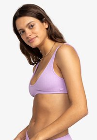 Paarse geribbelde bikini-top met een diepe halslijn en brede bandjes, met een klein label aan de zijkant. Glad textuur.
