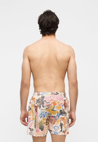 Homme aux cheveux foncés vu de dos portant un short de bain coloré avec des motifs abstraits d'océan et de nature.