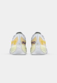 Pár bílých a žlutých běžeckých bot Puma zobrazený zezadu s textem "FLEX PRO" na oblasti paty na bílém pozadí.