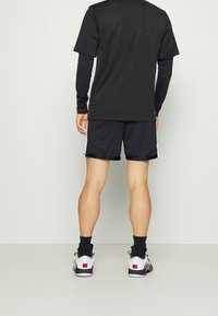 Zwarte sportshorts en een bijpassend T-shirt met korte mouwen van een textuurstof. Zwarte sokken en witte schoenen met rode accenten maken de outfit compleet.