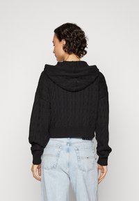 Crna skraćena dukserica s pletenim uzorkom i širokom kapuljačom te rebrastim manžetama. Upari s svijetloplavim trapericama visokog struka s stražnjim džepovima.