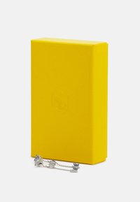 Gul texturerad låda med en präglad emblemet, prydd med en silverkedja med dekorativa inslag. Stängd med ett platt lock och snedställda kanter.