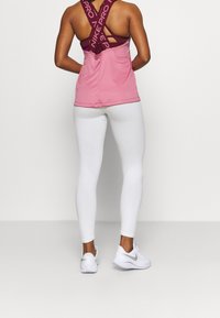 Růžový sportovní top s otevřenými zády a vínovou vnitřní vrstvou, doplněný úzkými bílými legínami a bílými teniskami se šněrováním na zádech.