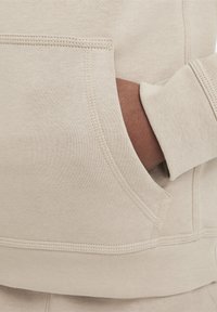 Hanorac bej cu buzunar tip cangur. Dispune de manșete și tiv ribbate, textură netedă și cusături detaliate de-a lungul îmbinărilor.