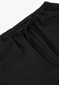 Pantalon noir avec ceinture élastique et cordon noué à l'avant, montrant la texture du tissu et les détails des coutures.