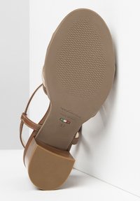 Sandale en cuir marron avec des sangles ajustables, semelle texturée et un talon carré. Présente le marquage de la marque et la taille 37 sur la semelle. Fabriquée en Italie.