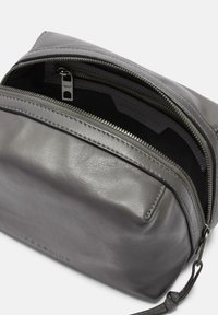 Neceser de cuero gris con un acabado suave, que cuenta con un cierre superior de cremallera y una tela interior de contraste, mostrando una etiqueta de la marca en su interior.