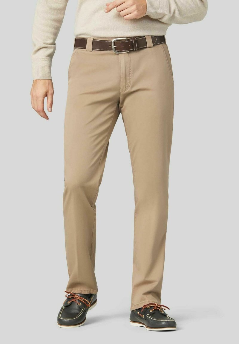Beige Chinos mit geradem Bein, aus einem Baumwollgemisch gefertigt. Ausgestattet mit einem braunen Gürtel mit einer silbernen Schnalle und akzentuiertem Schuhwerk.