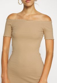 Robe marron clair à épaules dénudées en tissu côtelé. Manches courtes aux bords festonnés, coupe ajustée, texture lisse.