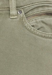 Close-up van kaki denimstof met voorzak met metalen klinknagel, riemlus en zichtbare messing rits.