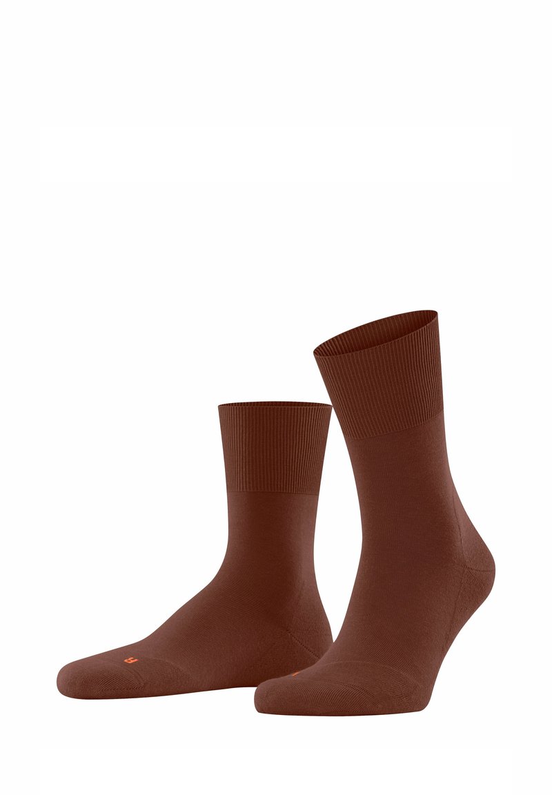 Chaussettes brunes jusqu'aux chevilles en matériau lisse et extensible. Présentent un bord côtelé et un logo discret en orange sur la semelle.