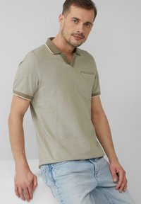 Oliwkowa koszulka polo z dekoltem w serek, krótkimi rękawami, kontrastowym białym wykończeniem na kołnierzyku i mankietach oraz małą kieszonką na piersi.
