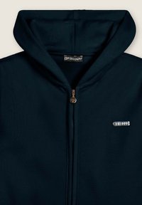 Felpa con zip di colore blu navy scuro, dotata di chiusura metallica e di un'etichetta con logo argento sulla parte sinistra del petto. Tessuto morbido con un cappuccio accogliente.