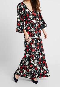 Blommig maxiklänning med svart bakgrund, prydd med röda och vita blommor, djup V-ringning, breda ärmar och knytmidja. Mjuk tyg.