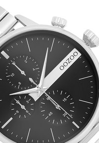 Montre chronographe en acier inoxydable argenté avec un cadran noir, trois sous-cadrans et des aiguilles argentées bien visibles. Présente un design épuré et minimaliste.