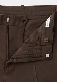 Ceinture de pantalon marron foncé avec fermeture éclair ouverte, bouton et crochet métallique montrant les coutures intérieures et l'étiquette en tissu.