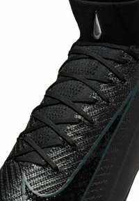 Schwarzer Sportschuh mit einer strukturierten synthetischen Oberseite, ausgestattet mit einem hohen Kragen, kompliziertem Schnürdesign und kontrastierenden grünen Akzenten.