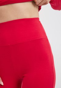 Czerwone legginsy o wysokim stanie z gładką fakturą, z subtelnymi detalami w przeszyciach i dopasowanym krojem w okolicy talii i bioder.