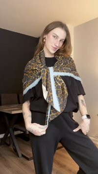 Schal mit Leopardenmuster und hellblauen, fransigen Kanten, um die Schultern drapiert. Wird über einem schwarzen Oberteil getragen und zeigt einen lässigen Stil.