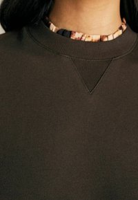 Sweatshirt marron foncé avec un col rond, présentant un col texturé aux motifs floraux contrastés. Tissu lisse avec une coupe classique.