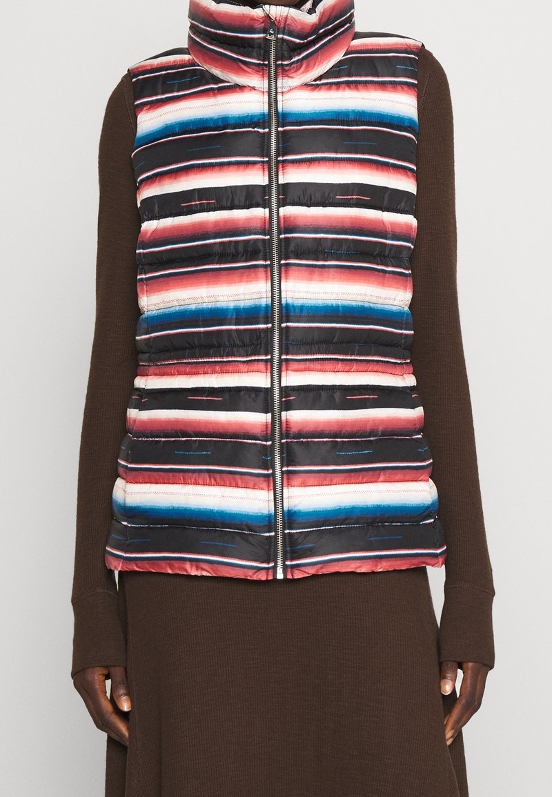 Vuorillinen hihaton liivi, jossa on monivärisiä vaakasuoria raitoja punaisena, sinisenä ja valkoisena mustalla taustalla. Siinä on korkea kaulus ja vetoketjukiinnitys.