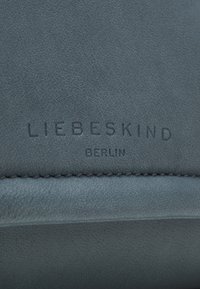 Pelle grigia texturizzata con una finitura liscia. Presenta il logo in rilievo "LIEBESKIND BERLIN". Cuciture visibili lungo il bordo.