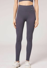 Dunkelviolette, gerippte Leggings mit hohem Bund, die einen engen Sitz und eine glatte Textur aufweisen, kombiniert mit weißen Sportschuhen.