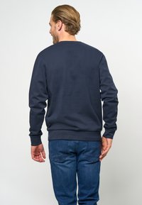 Marineblauwe sweatshirt met een ronde hals, geribbelde manchetten en stretchband. Zachte textuur met een eenvoudig ontwerp, gecombineerd met blauwe spijkerbroeken.