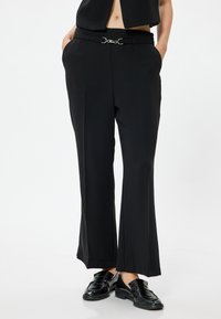 Svart skräddarsydda byxor med rak benprofil, med en silverfärgad bältesknopp och fickor. Tillverkade av ett mjukt och lätt tyg.