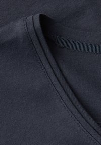 Tmavě námořnická modrá látka s hladkým povrchem, opatřená výstřihem do V a šitými okraji. Zoomovací záběr zdůrazňuje detaily švů.