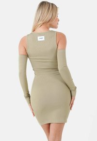 Abito color khaki a coste con maniche lunghe, silhouette aderente e un'etichetta quadrata sul retro. Texture liscia e design di lunghezza media.