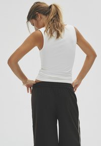Weißes, enganliegendes Tanktop mit glatter Textur, kombiniert mit lockeren schwarzen Hosen. Der Bund ist elastisch und sorgt für eine entspannte Silhouette.