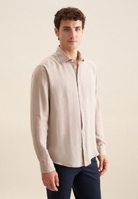 Lichtbeige langemouwen shirt van textuurstof; heeft een puntige kraag en een knoopsluiting aan de voorkant. Draag het met donkerblauwe broek.