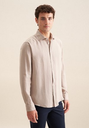 Lichtbeige langemouwen shirt van textuurstof; heeft een puntige kraag en een knoopsluiting aan de voorkant. Draag het met donkerblauwe broek.