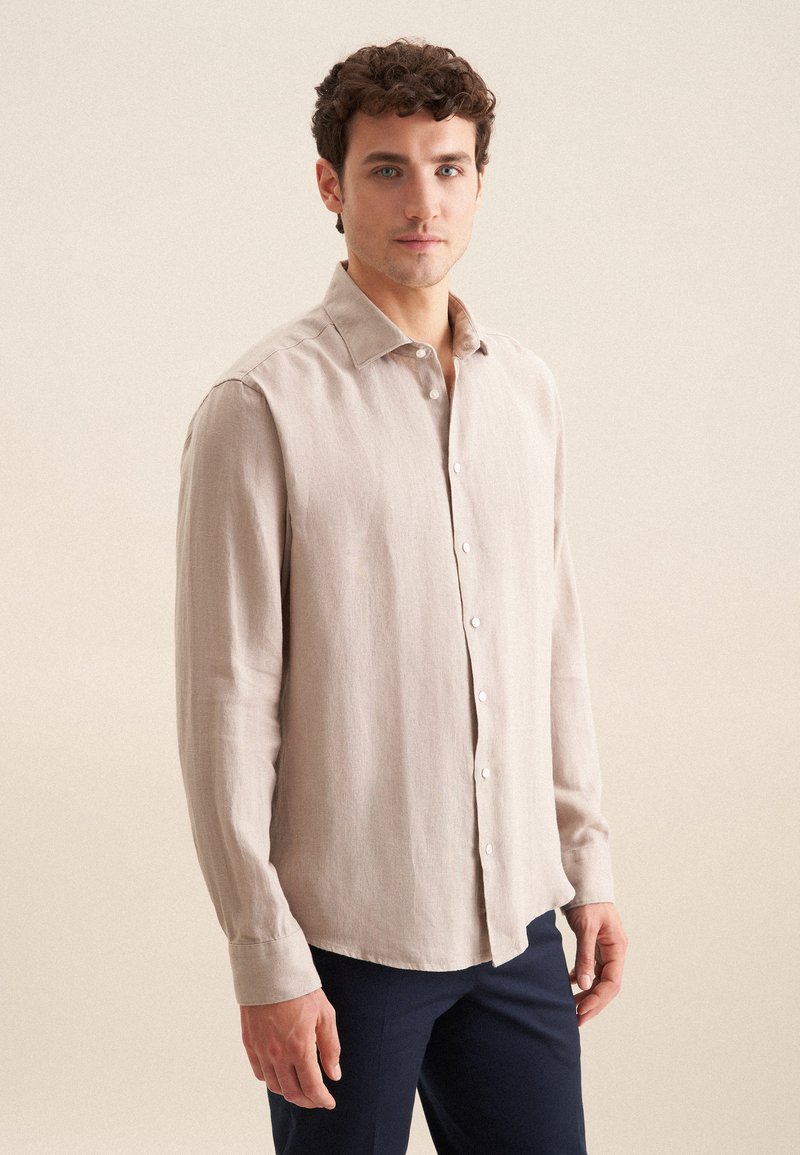 Lichtbeige langemouwen shirt van textuurstof; heeft een puntige kraag en een knoopsluiting aan de voorkant. Draag het met donkerblauwe broek.