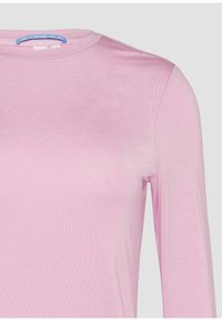 Lichtroze langemouwen top van een zachte, gladde stof. Bevat een ronde halslijn en een subtiele ribbeltextuur met een label waarop staat: "PLEZIER IS WAAR JIJ BENT."