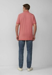 Rosa Poloshirt mit kurzen Ärmeln, lockere Passform, getragen mit blauen Jeans und weißen Sneakers, von hinten betrachtet.