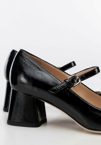 Scarpe Mary Jane in vernice nera con tacco quadrato, due cinturini sottili con fibbie e una finitura lucida e testurizzata.