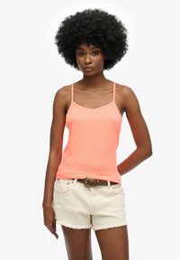 Camisola rosa neon con spalline sottili, abbinata a pantaloni corti bianchi strappati e una cintura marrone. Texture liscia e design casual.