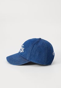 Denim baseball cap with a curved brim, blue color, featuring white embroidered text on the front and a rounded top with stitching details.