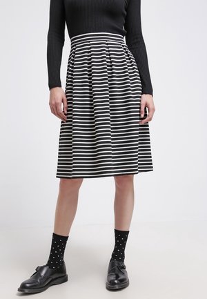 Kobieta ubrana w spódnicę z czarno-białymi poziomymi paskami, czarną bluzkę z długim rękawem, czarne skarpetki w grochy oraz czarne buty z klamrą.