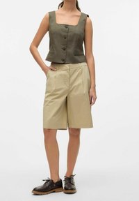 Oliwkowy krótki top z kwadratowym dekoltem i zapięciem na guziki, w połączeniu z beżowymi spódniczkami w pliski. Brązowe buty na sznurówki dopełniają całość.