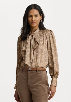 Brun mønstret bluse med sløyfe, med puffede ermer. Blandede teksturer med glatt stoff. Brune corduroy bukser med belte.