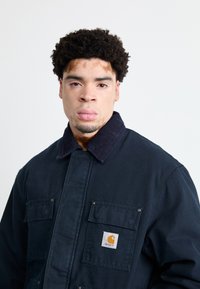Marineblaues Arbeitsjackett aus strapazierfähigem Stoff, mit einem Cordkragen, zwei Brusttaschen und einem Logopatch auf der linken Tasche.