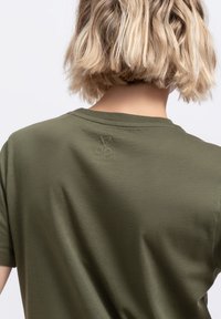 Olijfgroene katoenen t-shirt met een ronde halslijn en korte mouwen. Heeft een subtiele schaarafbeelding die is ingebed op de bovenrug.