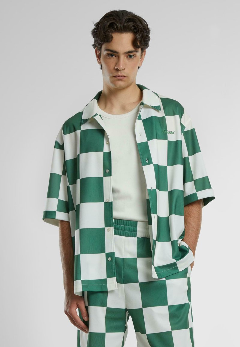 Camicia a quadri verde e bianca con maniche corte, chiusura a bottoni e colletto rilassato, abbinata a pantaloni a quadri coordinati.